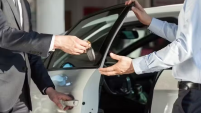 Duas pessoas entregam a chave de um carro branco com a porta aberta.
