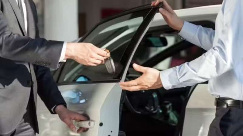 Duas pessoas entregam a chave de um carro branco com a porta aberta.